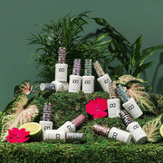 Collection of nail polish bottles arranged on a green surface with plants and flowers.